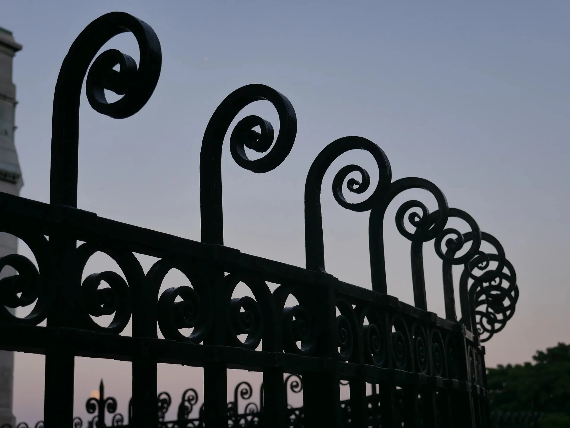 Grille artistique en fer forgé à spirales en silhouette au crépuscule parisien