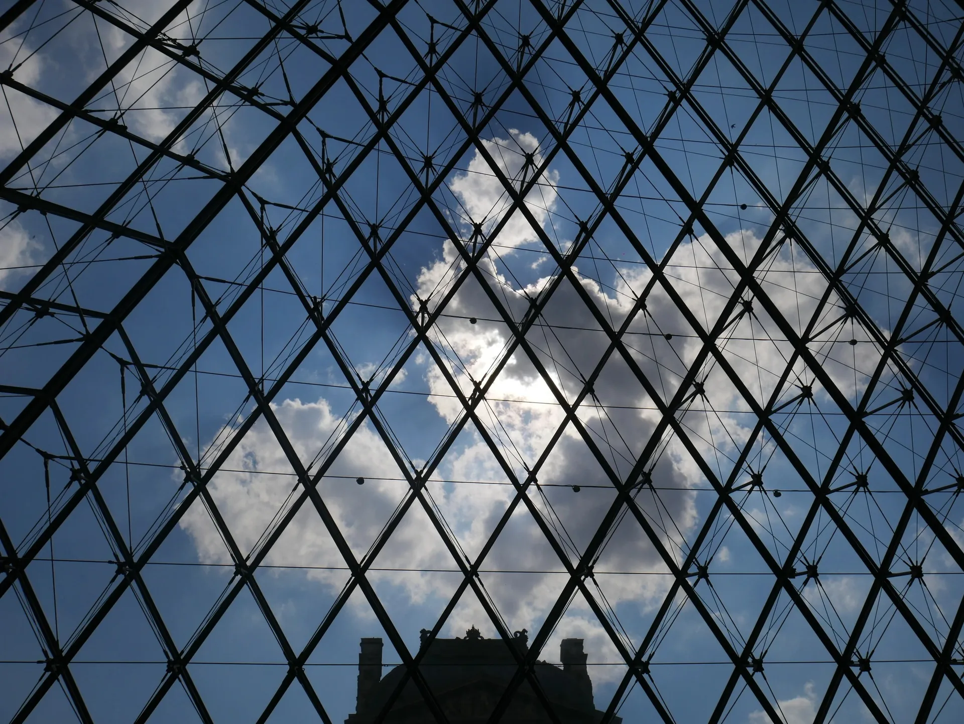 Intérieur de la pyramide du Louvre avec structure métallique et ciel nuageux