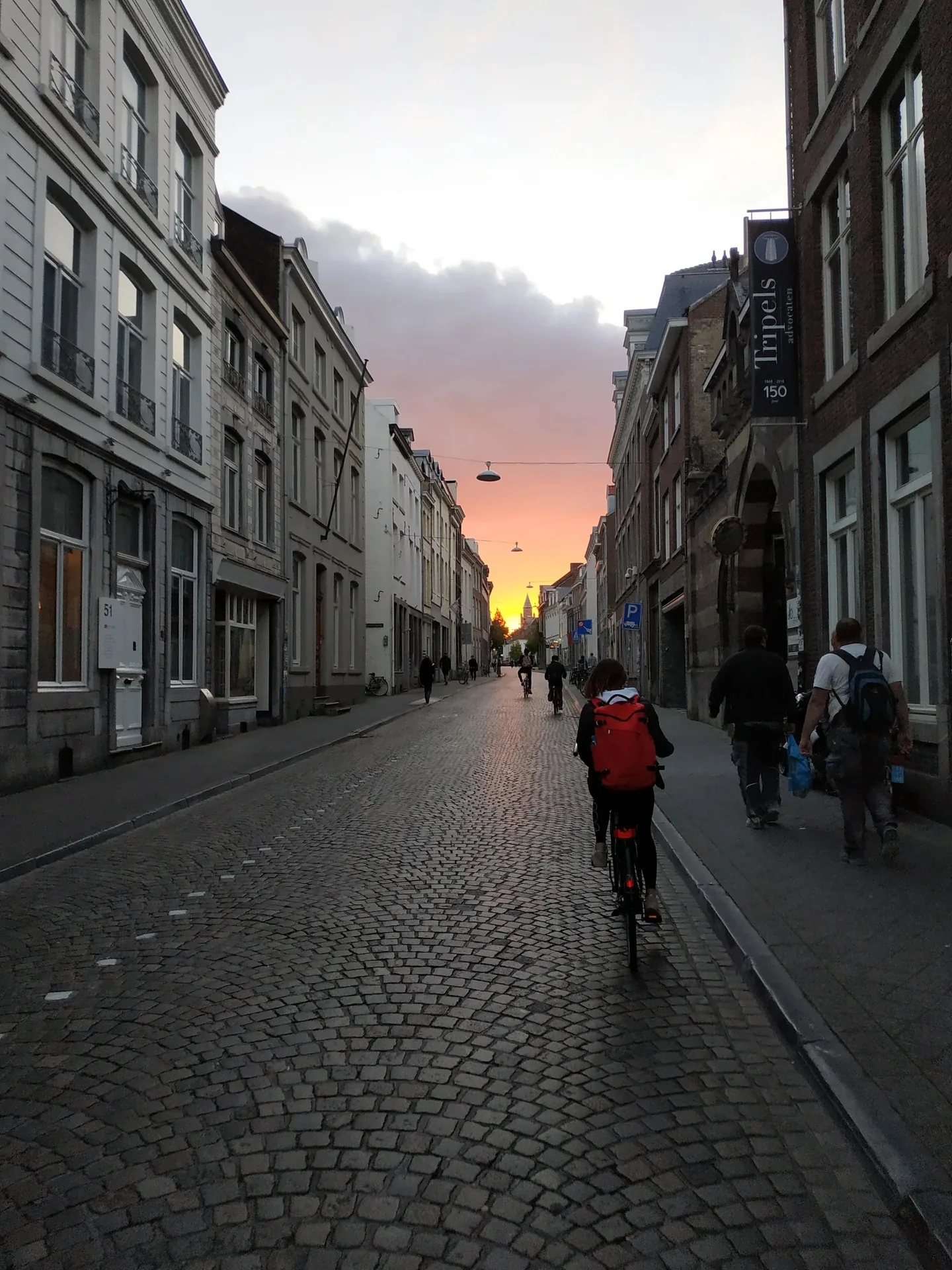 Rue pavée de Maastricht avec cyclistes sous un coucher de soleil rose